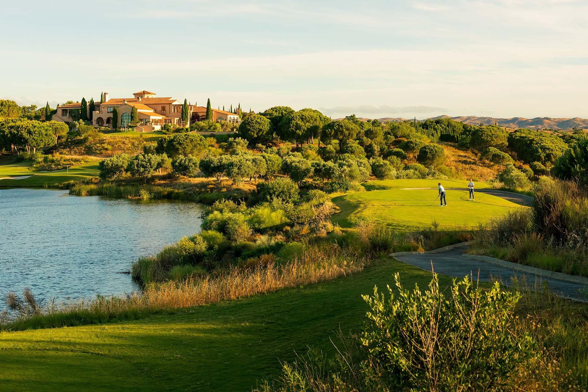 Lakeside green with golfers and the Monte Rei clubhouse beyond