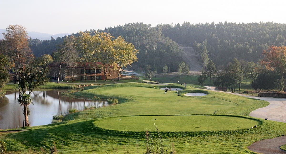 Tee box and green beside a lake with the stone clubhouse behind at Vale Pisão